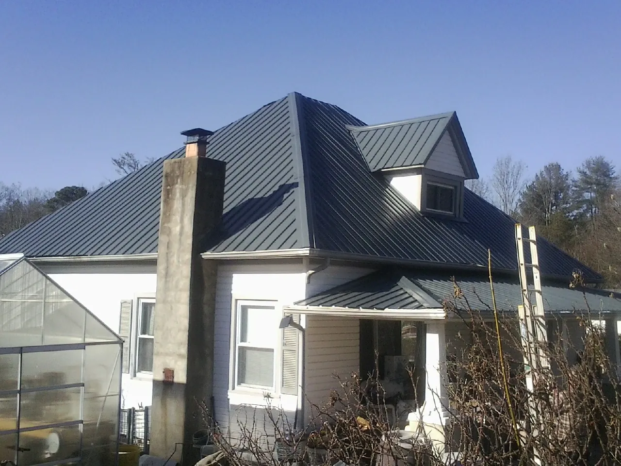 Dark blue standing seam metal roof on a white farmhouse with dormer — Slate & Tile Roof Repair by Roofing Brothers in Pauls Valley
