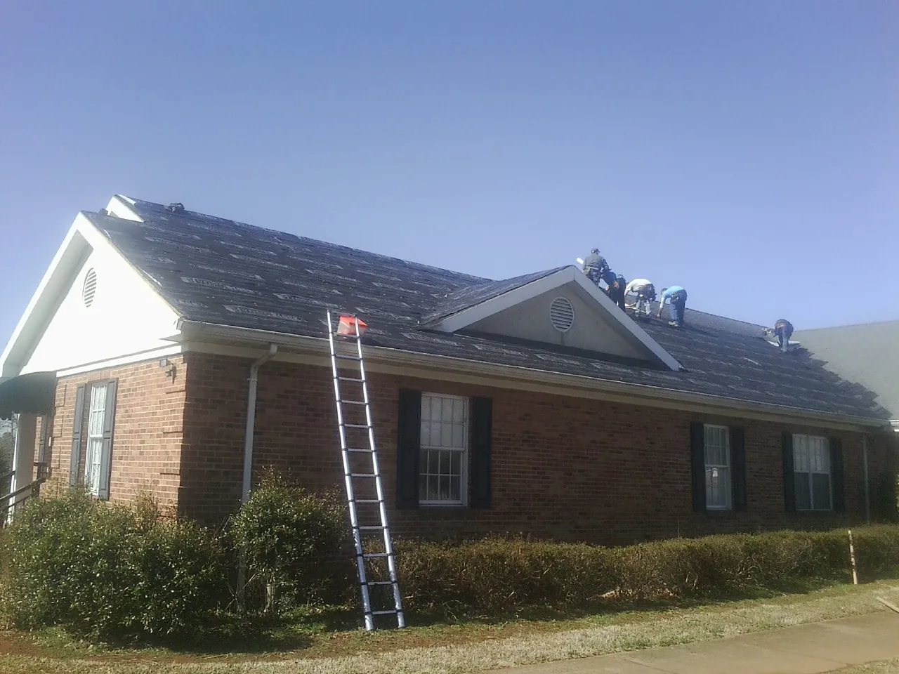 Crew tearing shingles off a brick ranch roof with a ladder set — Emergency Roof Repair work by our crew in Pauls Valley