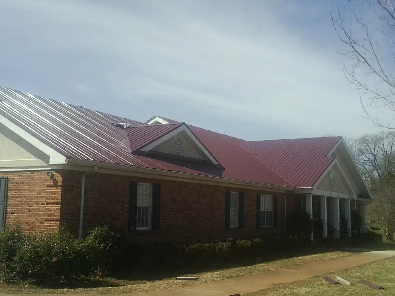Red metal roof with gabled entries on a long brick building, from a Hail Damage Roof Repair job in Pauls Valley