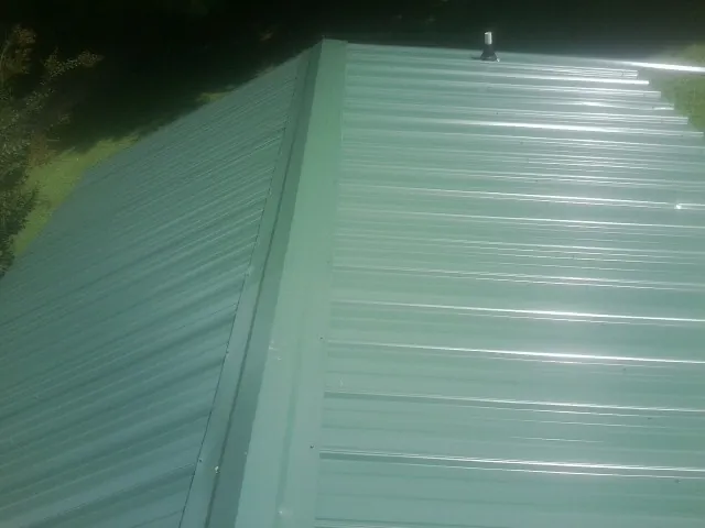 New green metal panels meeting at the ridge of a roof — Flat Roof Repair work by our crew in Pauls Valley