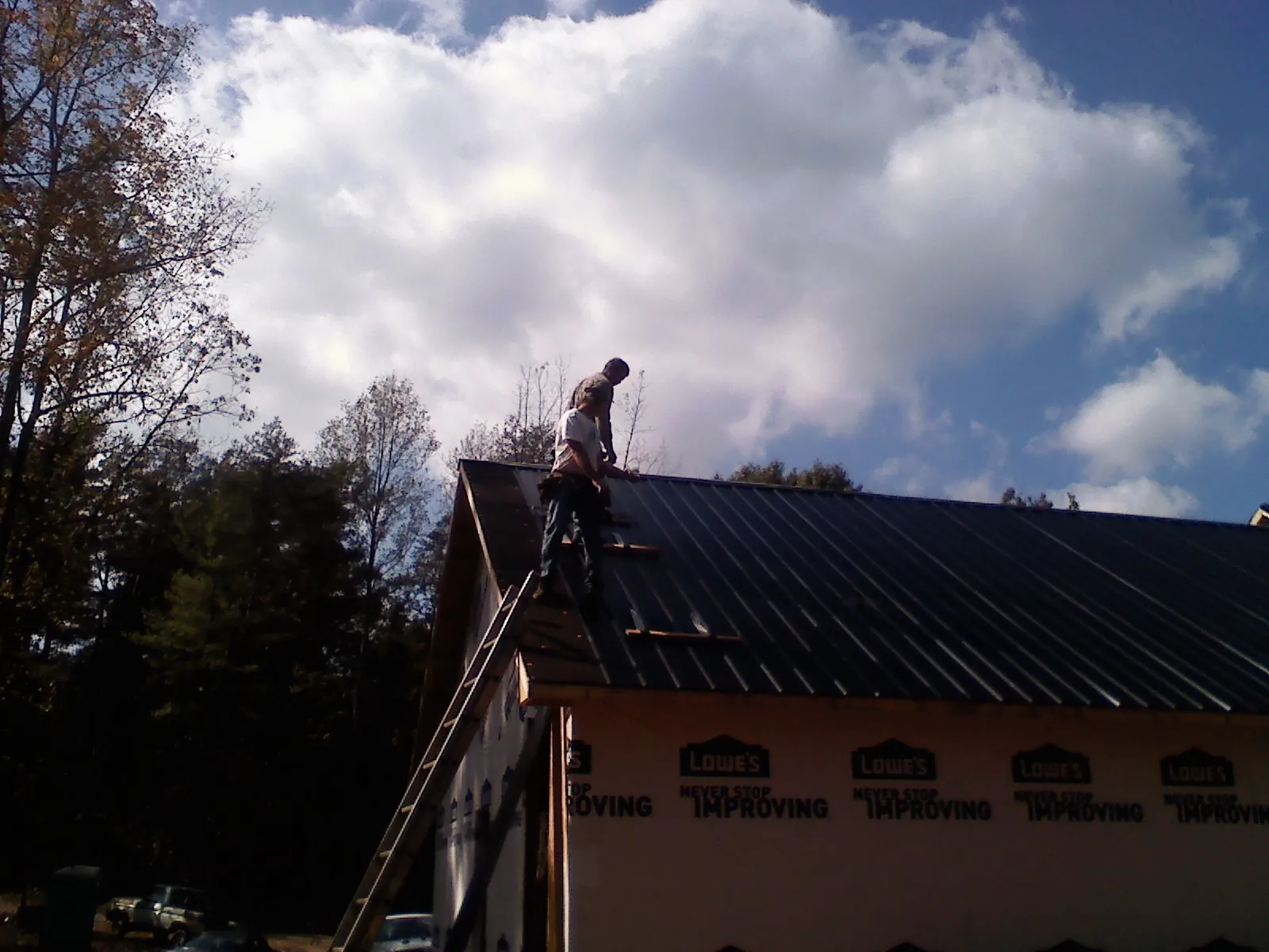 Roofer fastening dark metal panels high against a cloudy sky, from a Roof Inspection job in Pauls Valley
