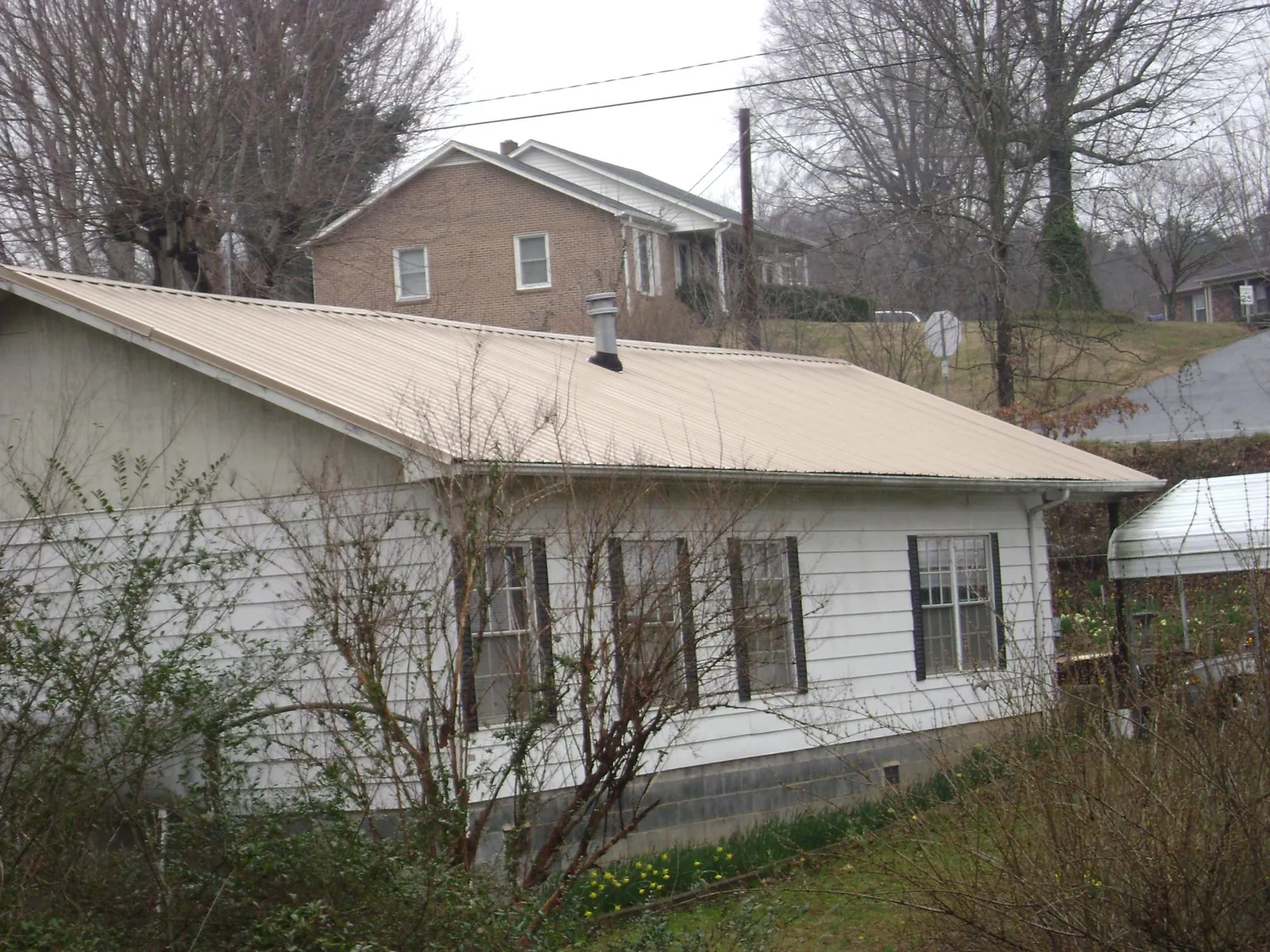 Tan metal roof on a white sided house set into a hillside — Commercial Roofing by Roofing Brothers in Pauls Valley