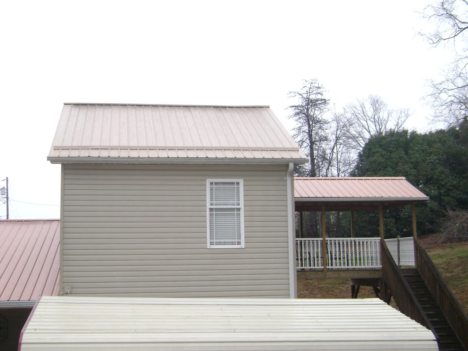 Tan metal roofs on a two story addition and attached porch, from a Roof Replacement job in Pauls Valley